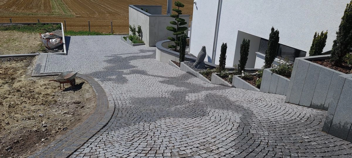 Geschwungener Natursteinpflaster-Weg mit Formgehölzen und Steinfigur am Gebäude