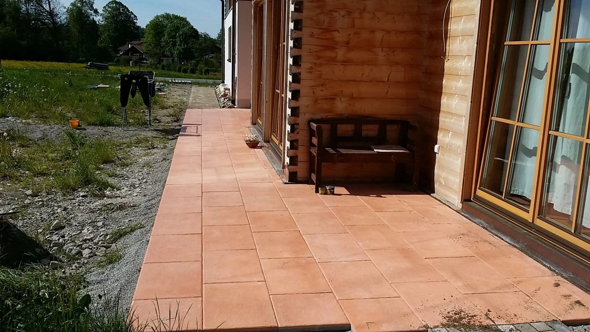 Terrasse aus Terracotta-Platten entlang eines Holzhauses mit Sitzbank