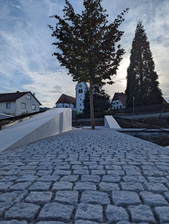 Gepflasterter Gehweg aus Naturstein mit Baum vor Kirche und Fachwerkhäusern